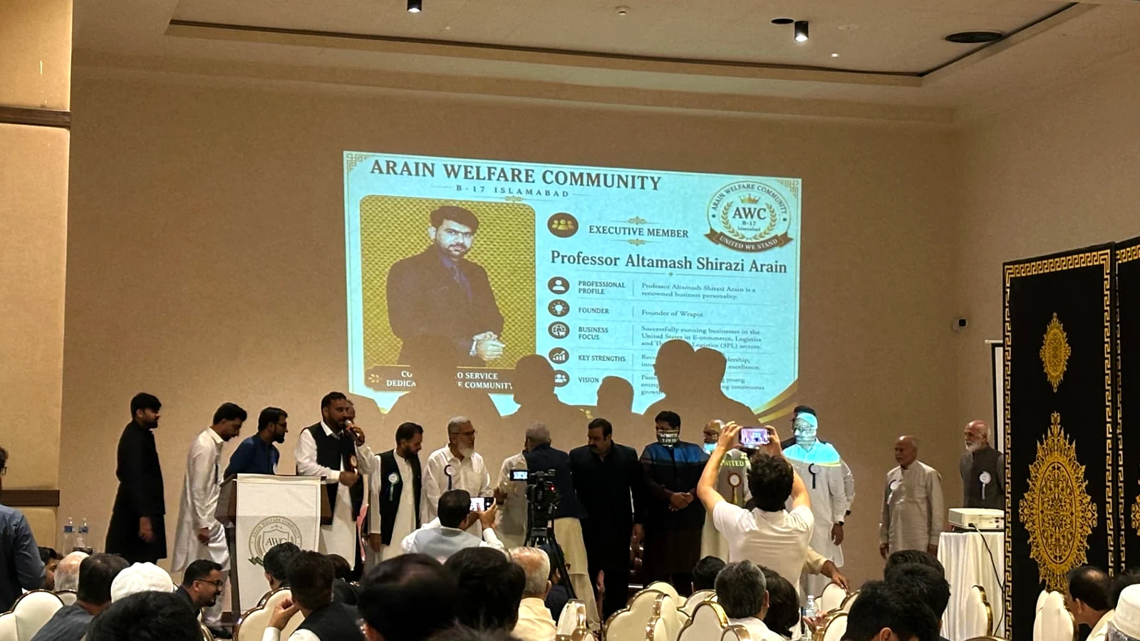 Executive members standing on stage as their profiles are presented on the screen behind them
