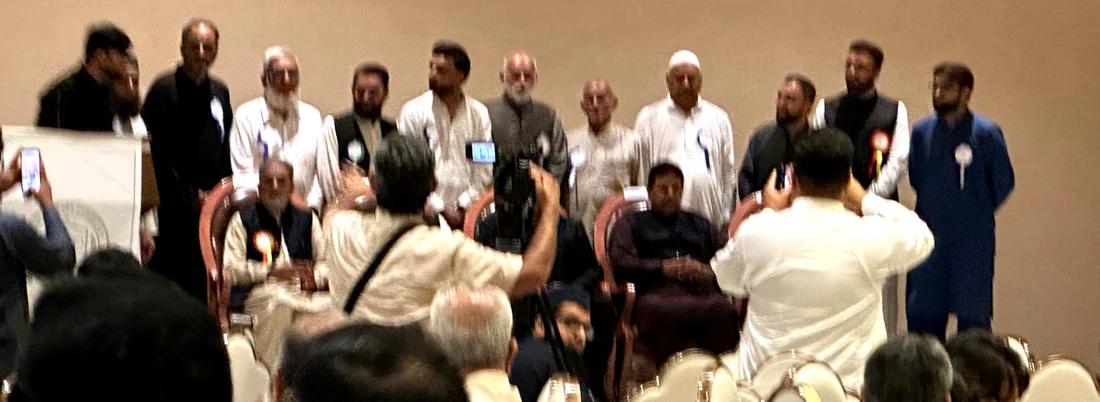 Elders and younger members of the Arain Welfare Community standing together on stage during a recognition segment